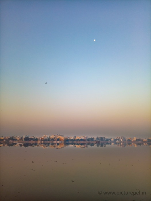 City skyline reflected in water at dawn with the moon visible