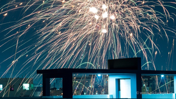 Fireworks exploding over a city rooftop at night
